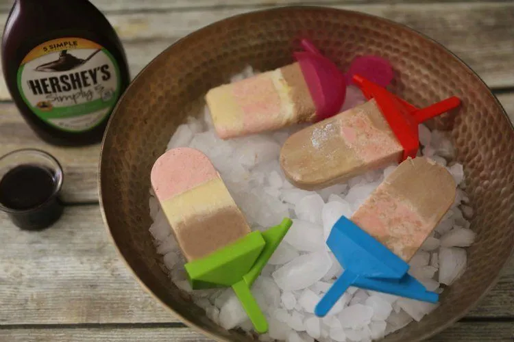 Easy Summer Recipes Roundup: Beat The Heat 16 Simple Recipes 16 A close-up of a layered banana split popsicles showing distinct layers of blended banana, strawberry, and chocolate swirl with bite taken out.