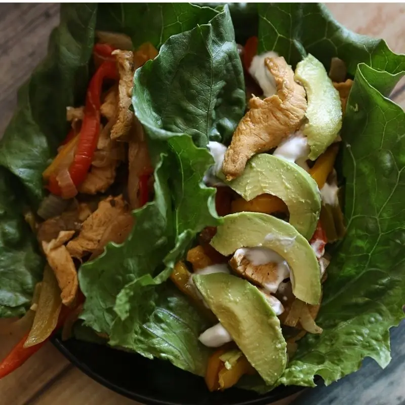 Delicious One Pan Chicken Fajita-ish Wraps: Beat The Diet Tax 11 A close up overhead shot of a healthy chicken fajita lettuce wrap loaded with peppers and onions, topped with sour cream and avocados. Half Baked Media