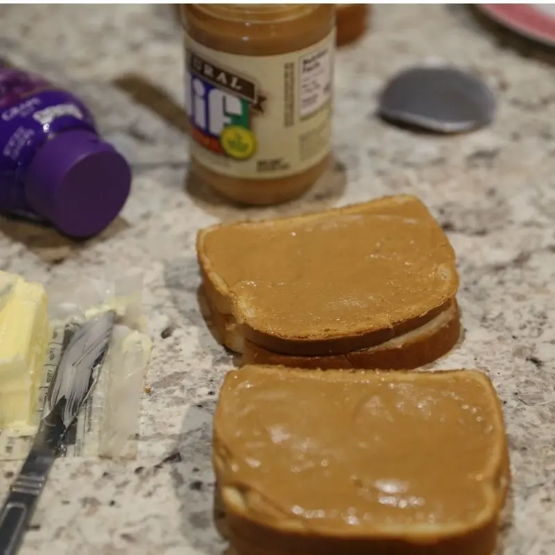 The Ultimate Grilled Peanut Butter and Jelly Sandwich Recipe 15 Two slices of white bread for a grilled peanut butter and jelly sandwich. Both slices are covered in a protective layer of creamy Jif peanut butter to prevent sogginess, with a thick scoop of Smucker’s grape jelly added to the center of one slice.