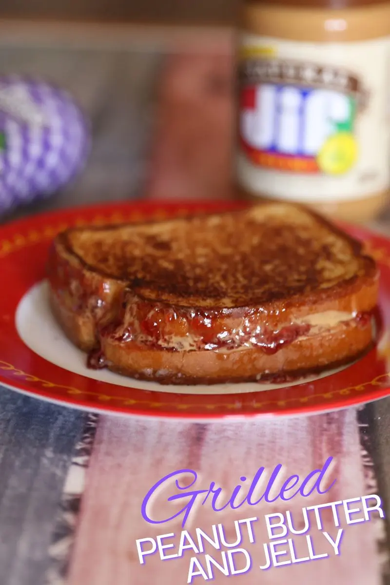 The Ultimate Grilled Peanut Butter and Jelly Sandwich Recipe 12 A perfectly toasted, golden-brown grilled peanut butter and jelly sandwich sliced in half on a red plate, showing the warm, melted Jif peanut butter and gooey Smucker's grape jelly oozing from the sides.